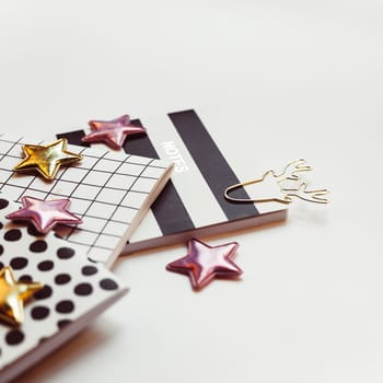 Desktop feminine composition with patterned notepads, golden stars and deer clips on white table with sun light and shadows. Close up concept for blogger