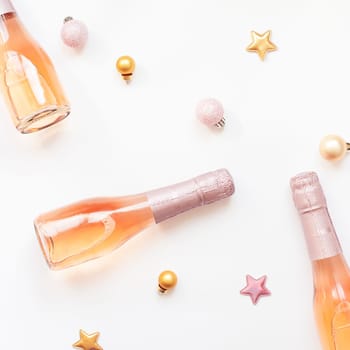 Christmas or New Year composition with bottles of rose champagne and golden shiny sparkle star confetti isolated on white background, top view. Celebration flat lay. Party creative concept