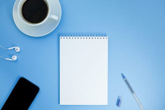 Creative flat lay photo of workspace desk with paper notebook, smartphone, earpieces, pen and coffee with copy space background minimal style