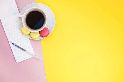 Creative flat lay photo of coffee cup with macaroons and a notepad with copy space on pink and yellow background minimal style