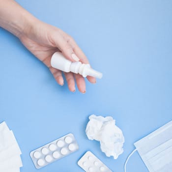 Creative flat lay concept of seasonal spring allergy with napkins, pills, face mask, drops in a bottle and a female hand with square copy space background minimal style, template for text