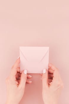 Creative image of woman hand holding small love letter with copy space on millennial pink background in minimalism style. Concept template for feminine blog, social media