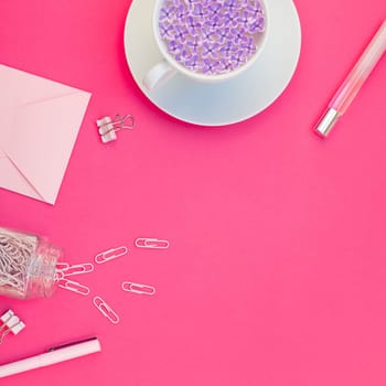 Top view flat lay of workspace desk styled design office supplies and cup of tea with copy space on a bright pink color paper background minimal style. Square Template for feminine blog social media
