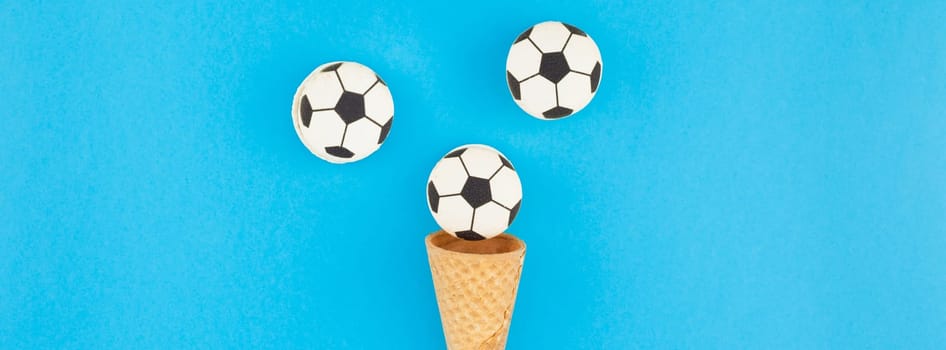 Long wide banner top view of ice cream waffle cones with soccer balls macarons on bright bold blue background with copy space in minimal style, concept of football games for children birthday