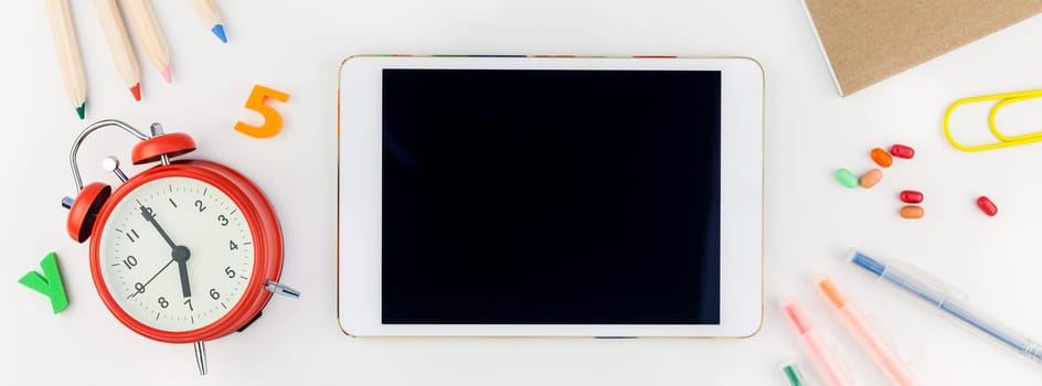 Long wide banner back to school concept blank tablet with alarm clock, color school and office supplies on white table background with copy space, frame, template for text or design