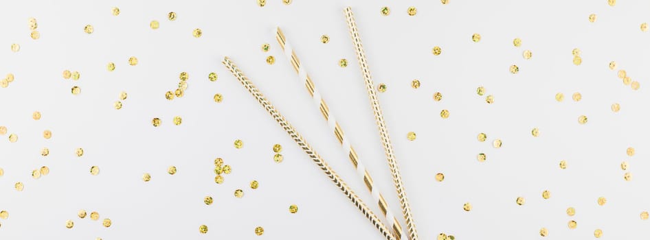 Holiday pattern flat lay top view Xmas Christmas New Year celebration drinking cocktail fun party straws golden sparkles glitter white background. Template for greeting card long wide banner