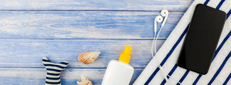 Long wide banner flat lay concept of summer travel vacations. Top view of beach towel smartphone seashells starfish on pastel blue wooden planks background with copy space mockup template for text