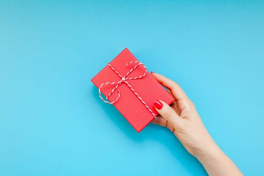 New Year Christmas Xmas Valentine birthday holiday celebration woman hand red manicure holding present gift box copy space turquoise blue color paper background minimal style. Template greeting card