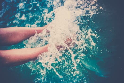 Female legs splashing sea water from a sailing yacht. Filtered shot