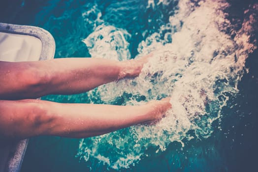 Female legs splashing sea water from a sailing yacht. Filtered shot