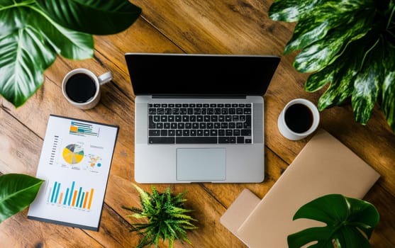 Overhead view of wooden desk with laptop, financial charts, coffee cups, and green plants, representing a contemporary home office setup for remote work and data analysis.