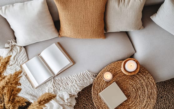 Inviting home interior featuring a comfortable sofa with pillows, open book, soft blanket, and glowing candles, creating a perfect atmosphere for relaxation and reading.
