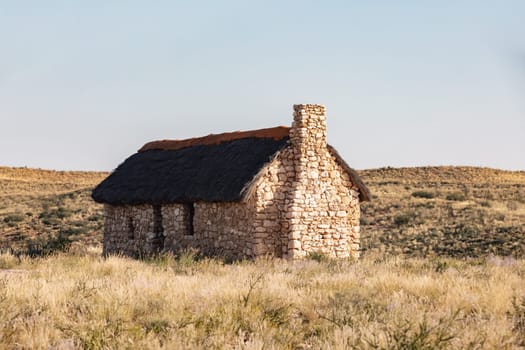 Alone stone house, weathered by the harsh elements, sits amidst the arid landscape of the Kalahari desert, South Africa
