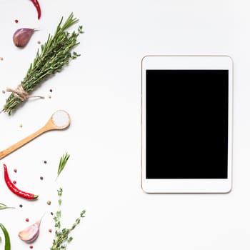 Flat lay overhead view tablet PC gadget mockup blank text space on white background with greens herbs and spices. Menu design food blog recipe cookbook or delivery app with cooking ingredients