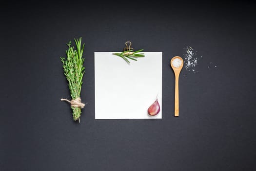 Flat lay overhead view blank recipe paper page with clip mockup text space invitation card on black background with greens herbs and spices. Menu recipe book food blog design with cooking ingredients