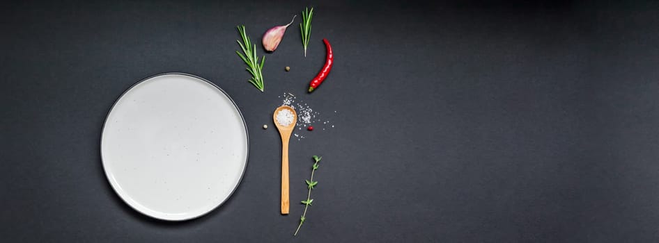 Flat lay overhead view empty plate mockup blank text space invitation card on black background with greens herbs and spices. Menu design food background with cooking ingredients