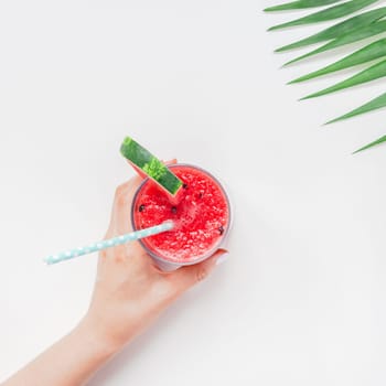 Creative scandinavian style flat lay top view of fresh watermelon slices smoothie drink in glass woman hands on white table background copy space. Minimal summer fruits concept for blog or recipe book