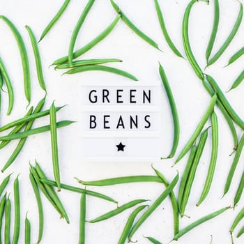 Creative scandinavian style flat lay top view of fresh green beans and text in lightbox on white concrete table background copy space. Minimal house cooking concept template for blog or recipe book