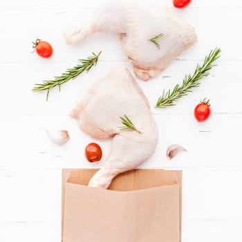 Creative Top view flat lay of fresh raw chicken legs with rosemary herbs garlic tomatoes on white wooden background with copy space. Food preparation recipe cooking concept