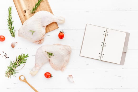 Creative Top view flat lay of fresh raw chicken legs with rosemary herbs garlic tomatoes on white wooden background with copy space. Food preparation recipe cooking concept