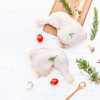Creative Top view flat lay of fresh raw chicken legs with rosemary herbs garlic tomatoes on white wooden background with copy space. Food preparation recipe cooking concept