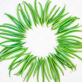 Creative scandinavian style flat lay top view of fresh green beans on white concrete table background copy space. Minimal house cooking concept template for blog or recipe book