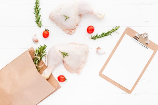 Creative Top view mock up flat lay of fresh raw chicken legs with rosemary herbs garlic tomatoes on white wooden background with copy space. Food preparation recipe cooking concept