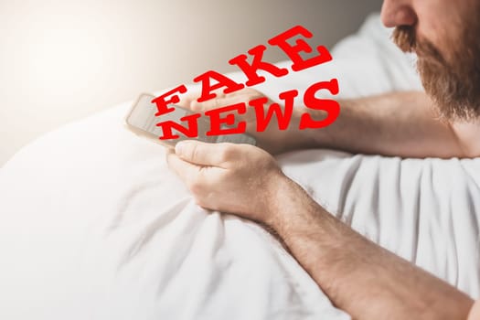 Fake news infodemics during Covid-19 pandemic concept. Man hands holding mobile phone reading global news or social net at home. Reading last news update in lockdown. Red text fake news on foreground