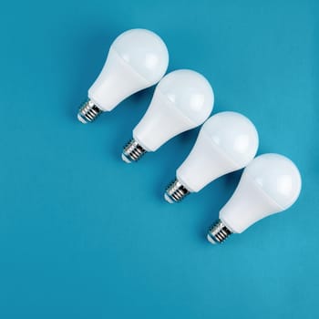 Energy-saving and eco-friendly life in conceptual frame pattern. Creative top view flat lay of LED light bulbs composition with copy space on blue background in minimal style.