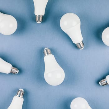 Energy-saving and eco-friendly life in conceptual frame pattern. Creative top view flat lay of LED light bulbs composition with copy space on blue background in minimal style.