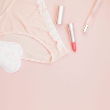 Square Feminine flat lay set of female panties and accessories, perfumes, lipstick and pads liners on pastel pink color background for fashion blog and social media with copy space for text