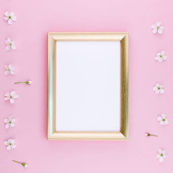 Square flat lay concept top view of blank frame mock up and cherry tree flowers on pastel millennial pink background with copy space in minimal style, template for lettering, text or design
