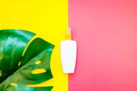 Tropical jungle palm monstera leaves and sunscreen blank bottle mockup on bright yellow and pink duotone paper background. Summer vacations creative flat lay concept template for text