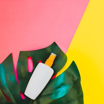 Tropical jungle palm monstera leaves and sunscreen blank bottle mockup on bright square yellow and pink duotone paper background. Summer vacations creative flat lay concept template for text