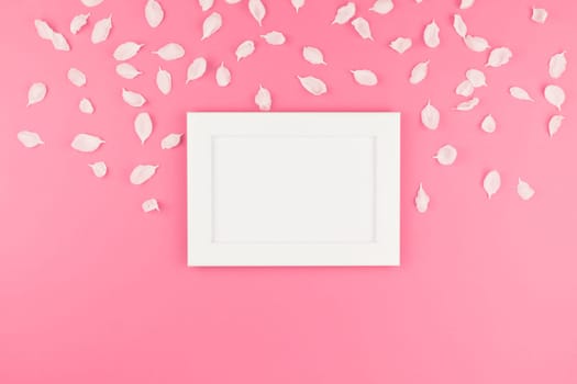Creative flat lay concept top view of white frame mock up and apple tree flowers petals on pastel pink background with copy space in minimal style, template for text