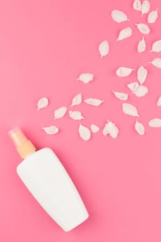 Flat lay set of sunscreen blank bottle mockup and white flowers petals on pastel pink color background for blog and social media with copy space for text