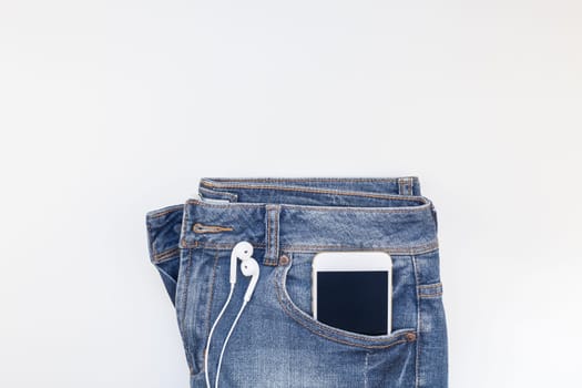 Flat lay of blue jeans and smartphone headphones isolated on white background with copy space. Overhead view of woman casual outfit. Trendy hipster look top view