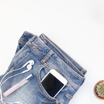Square Flat lay of blue jeans, bracelets cactus and smartphone with headphones on white background with copy space. Overhead view of woman casual outfit. Trendy hipster look top view