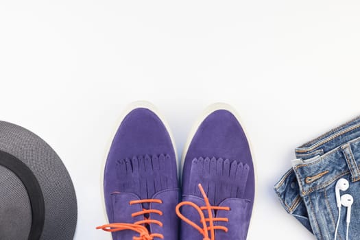 Flat lay of suede shoes, blue jeans, grey hat, cactus and smartphone with headphones on white background with copy space. Overhead view of woman casual outfit. Trendy hipster look top view