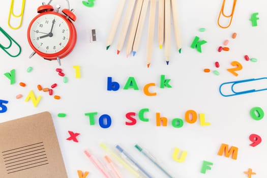 Creative flat lay back to school concept with alarm clock, color school and office supplies on white table background with copy space, frame, template for text or design