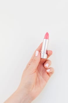 Woman hand with pastel manicure polish holding pink lipstick isolated on white background with copy space. Template for feminine beauty blog social media