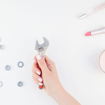Creative square image of woman hand with pastel manicure polish holding spanner with copy space nuts and cosmetics isolated white background in minimalism style. Repair or improvement feminism concept