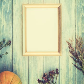 Square Top view of autumn orange pumpkins and dry flowers with grass thanksgiving background over blue toned wooden table with golden frame mock up and copy space in rustic style, template for text