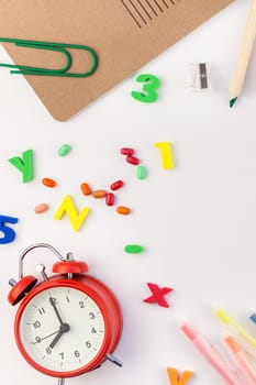 Creative flat lay back to school concept with alarm clock, color school and office supplies on white table background with copy space, frame, template for text or design