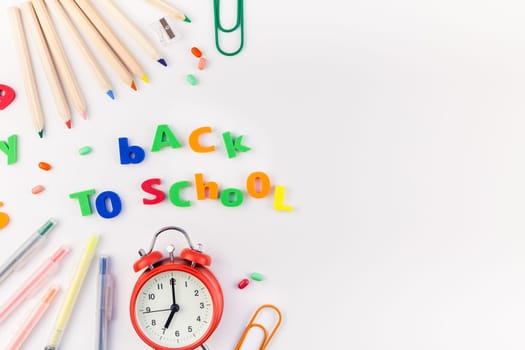 Creative flat lay back to school concept with alarm clock, color school and office supplies on white table background with copy space, frame, template for text or design