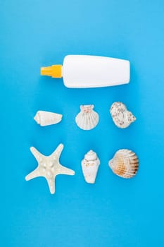 Creative flat lay concept of summer travel vacations. Top view of seashells and starfish on turquoise blue background with sunscreen blank bottle mock up and copy space in minimal style