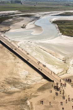 View from walls of Mont Saint Michel on the bay during the low tide. Groups of tourists walking. France