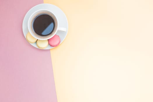 Creative flat lay photo of coffee cup and macaroons with copy space on pink and yellow background minimal style