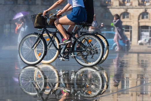 FRANCE, BORDEAUX - SEPTEMBER 20: People riding bicycles in the mirror fountain in front of Place de la Bourse in Bordeaux, France on September 20, 2015