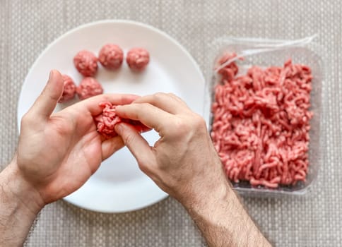 Man hands preparing meatballs with raw mincemeat. Lifestyle close up composition with natural light. Homemade cooking during lockdown, stay home housekeeping sharing concept. Top view